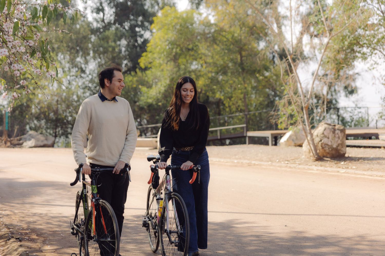 Happy couple walking side by side with bikes in a sunny outdoor park.
