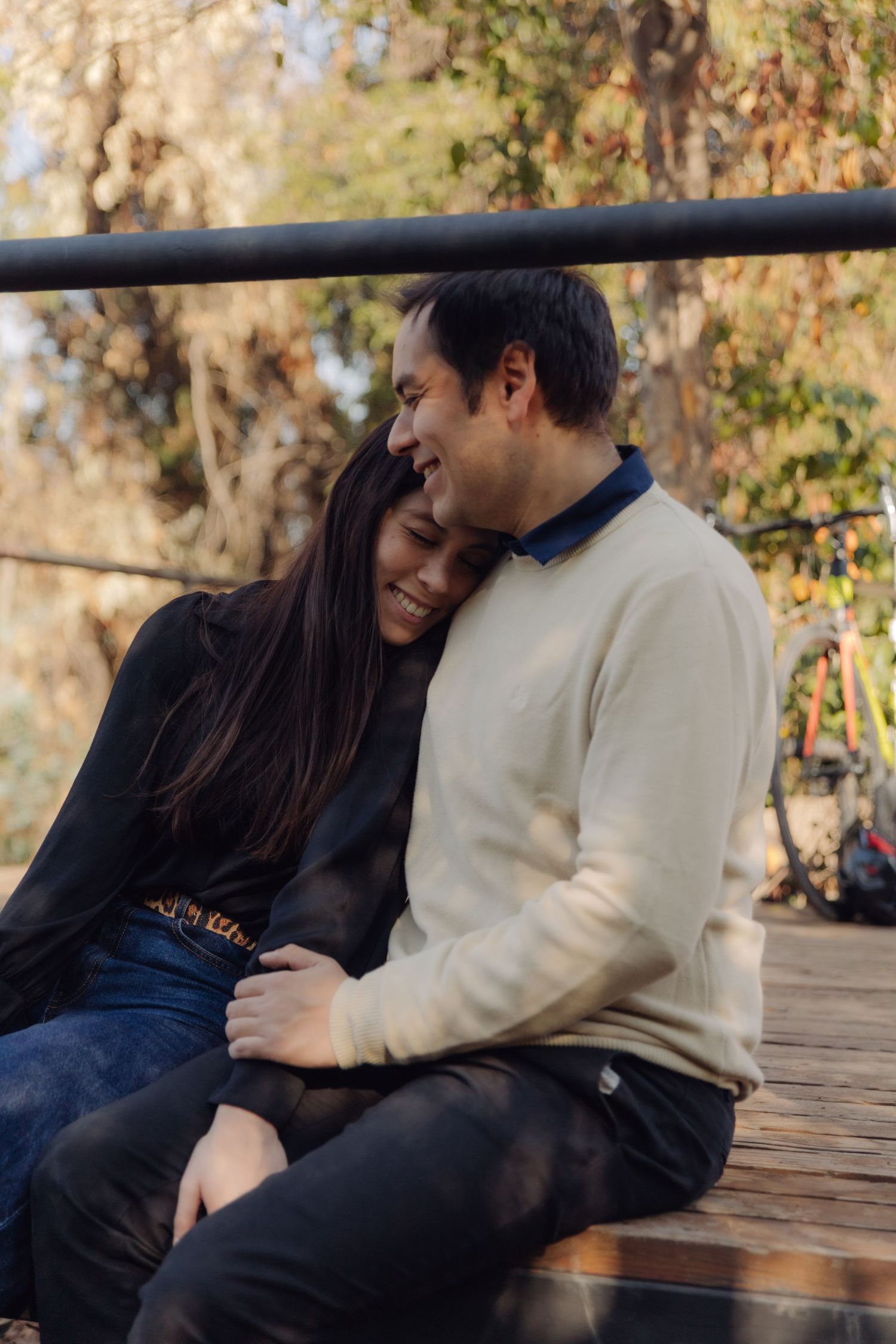 Man embracing laughing woman on a wooden bench in a sunlit park.