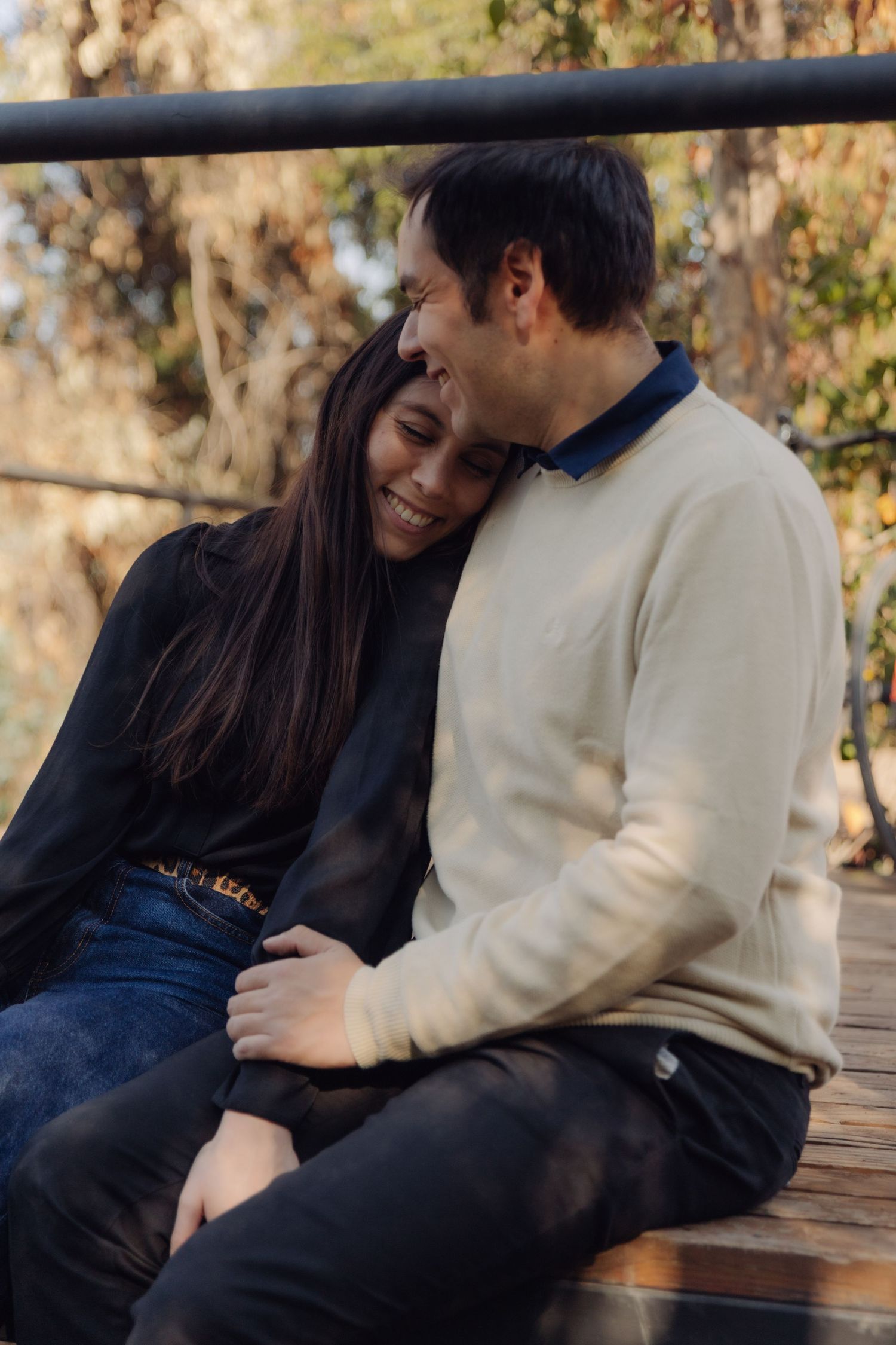 Couple cuddling and smiling together on a bench in a warm autumn park.