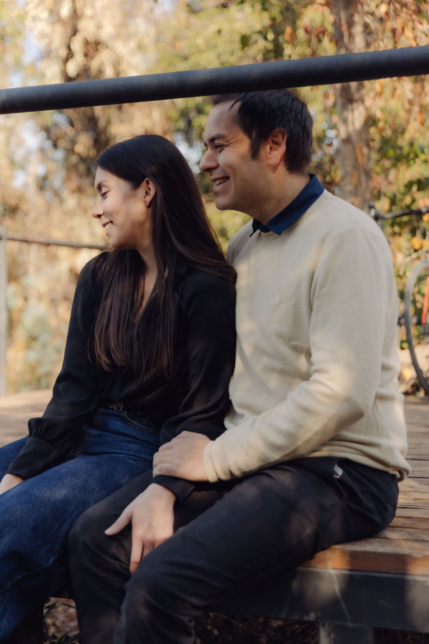 Happy couple sitting together on a bench laughing in a golden autumn park.