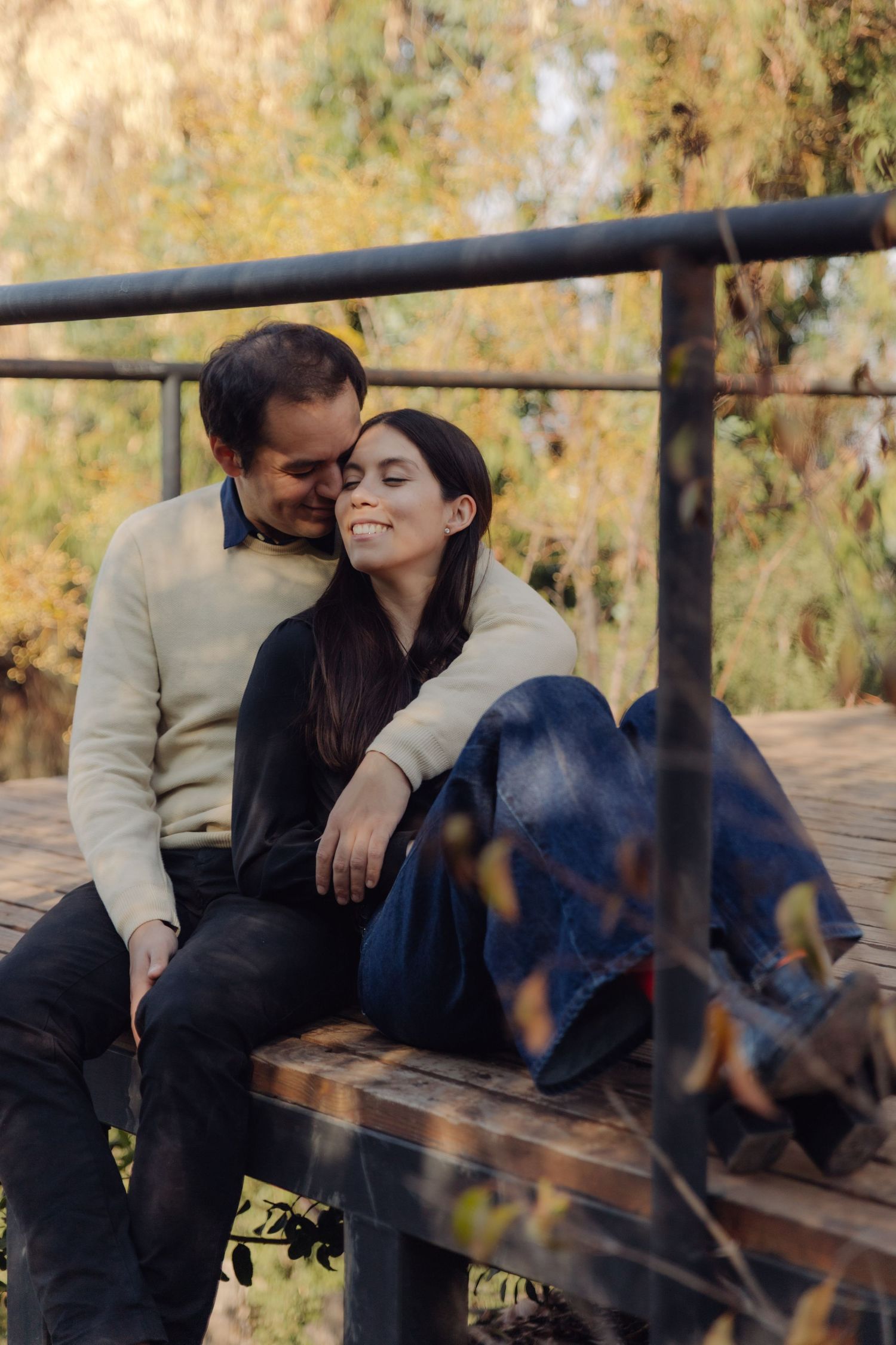 Romantic couple sharing a tender moment on a park bench, woman smiling with eyes closed as man leans in close.