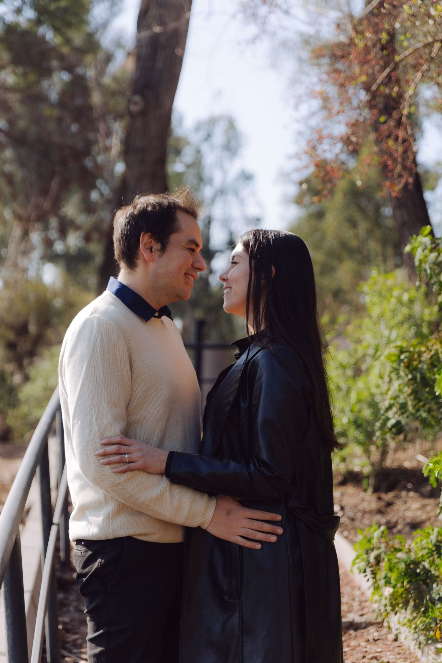 Happy couple embracing and smiling at each other on a wooden bridge in a sunny park.