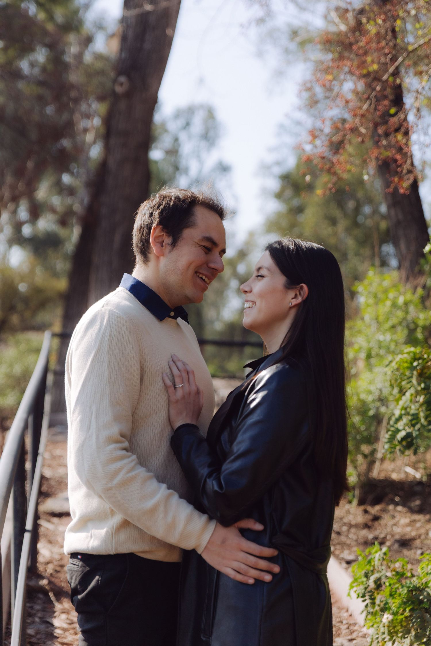 Joyful couple laughing and holding each other close on a sunlit park path with tall trees.