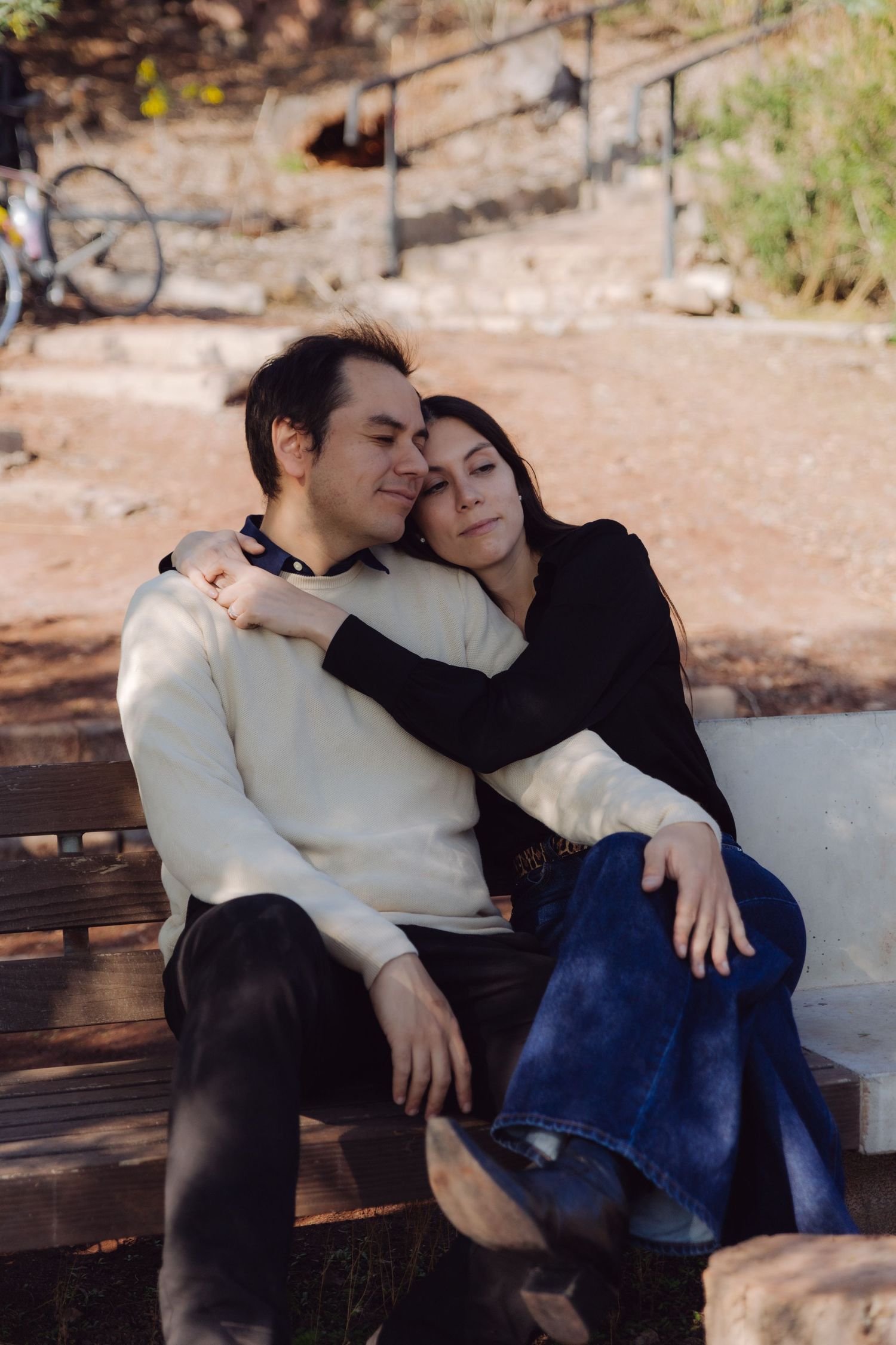 Couple sitting closely on a park bench, woman resting her head on mans shoulder affectionately.