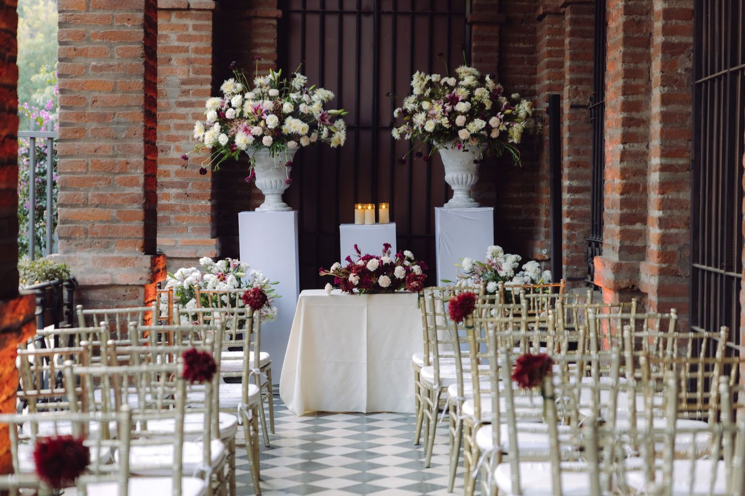 Outdoor wedding ceremony setup with white chairs, floral arrangements, candles, and large urn centerpieces.