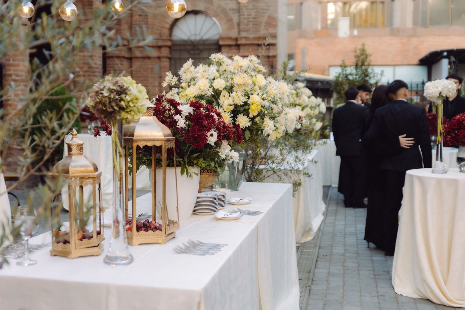Elegant wedding reception table with gold lanterns and lush floral arrangements of white and burgundy flowers.