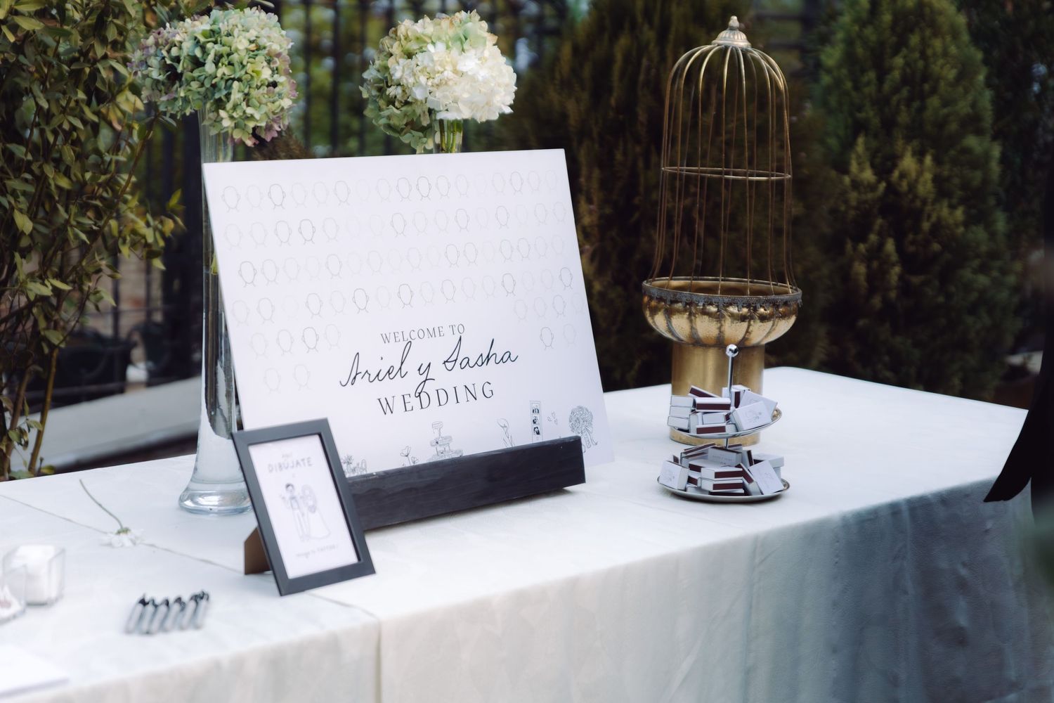 Elegant wedding welcome table with white floral arrangements, signage, and a decorative gold birdcage.