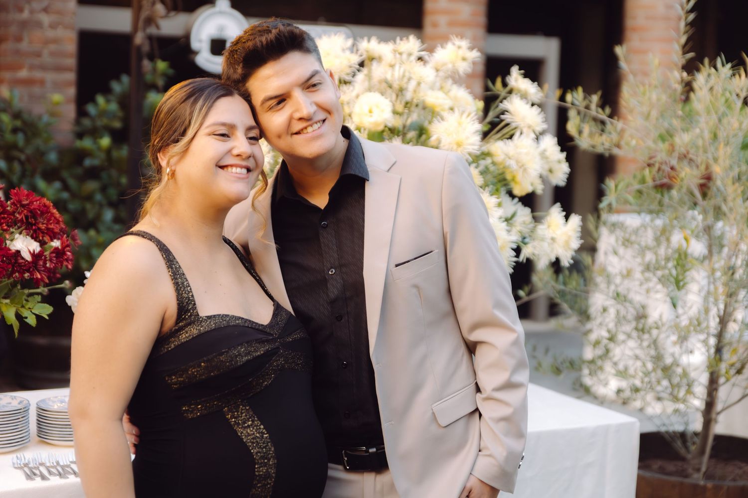 A smiling couple poses together at a wedding reception with white floral arrangements in the background.