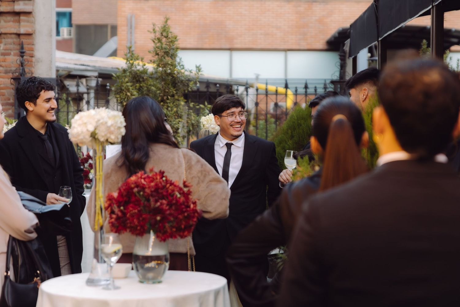 Guests mingle at an outdoor wedding cocktail hour with floral centerpieces and string lights.