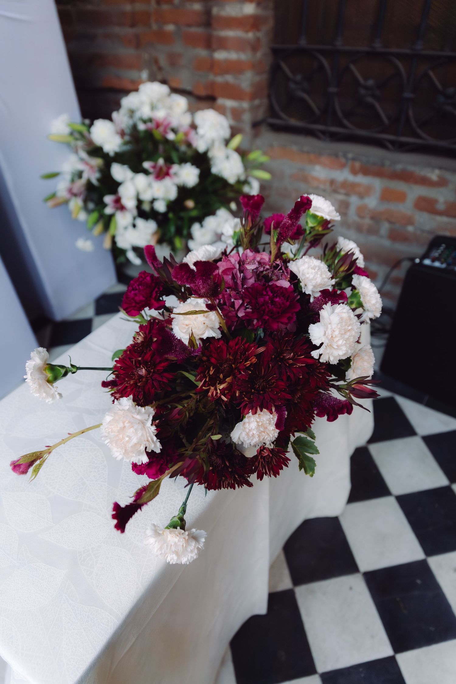 Elegant burgundy and white floral bouquet arrangement on a marble surface with checkered floor.