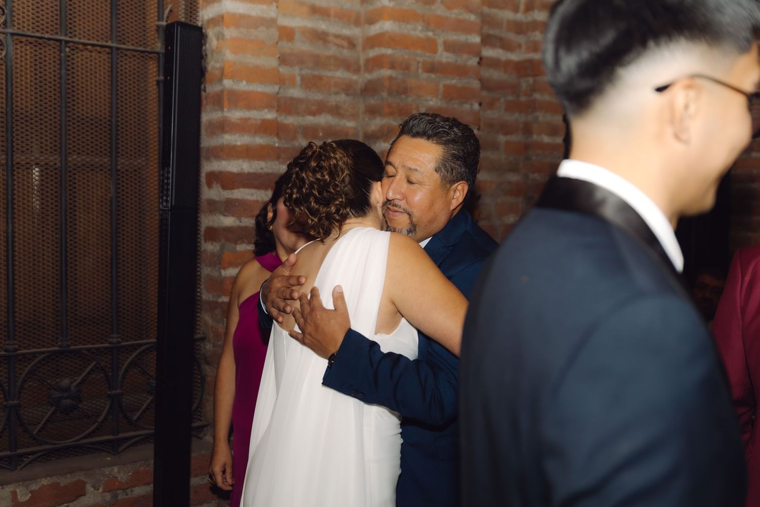 Bride in white gown receives heartfelt hug from family member at elegant wedding celebration.