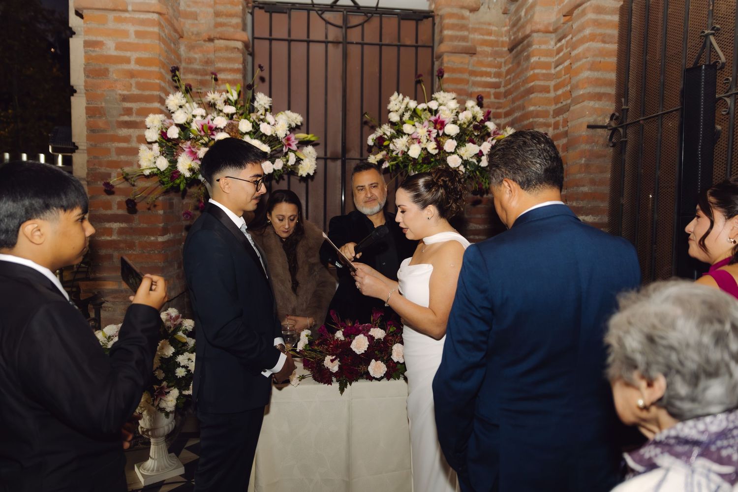 Bride reading vows to groom at romantic wedding ceremony with pink and white flower arrangements.
