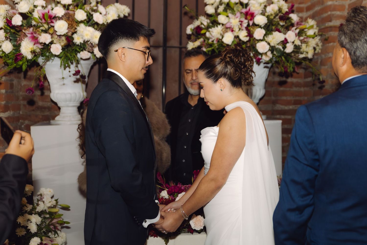 Bride and groom holding hands and facing each other during intimate indoor wedding ceremony.