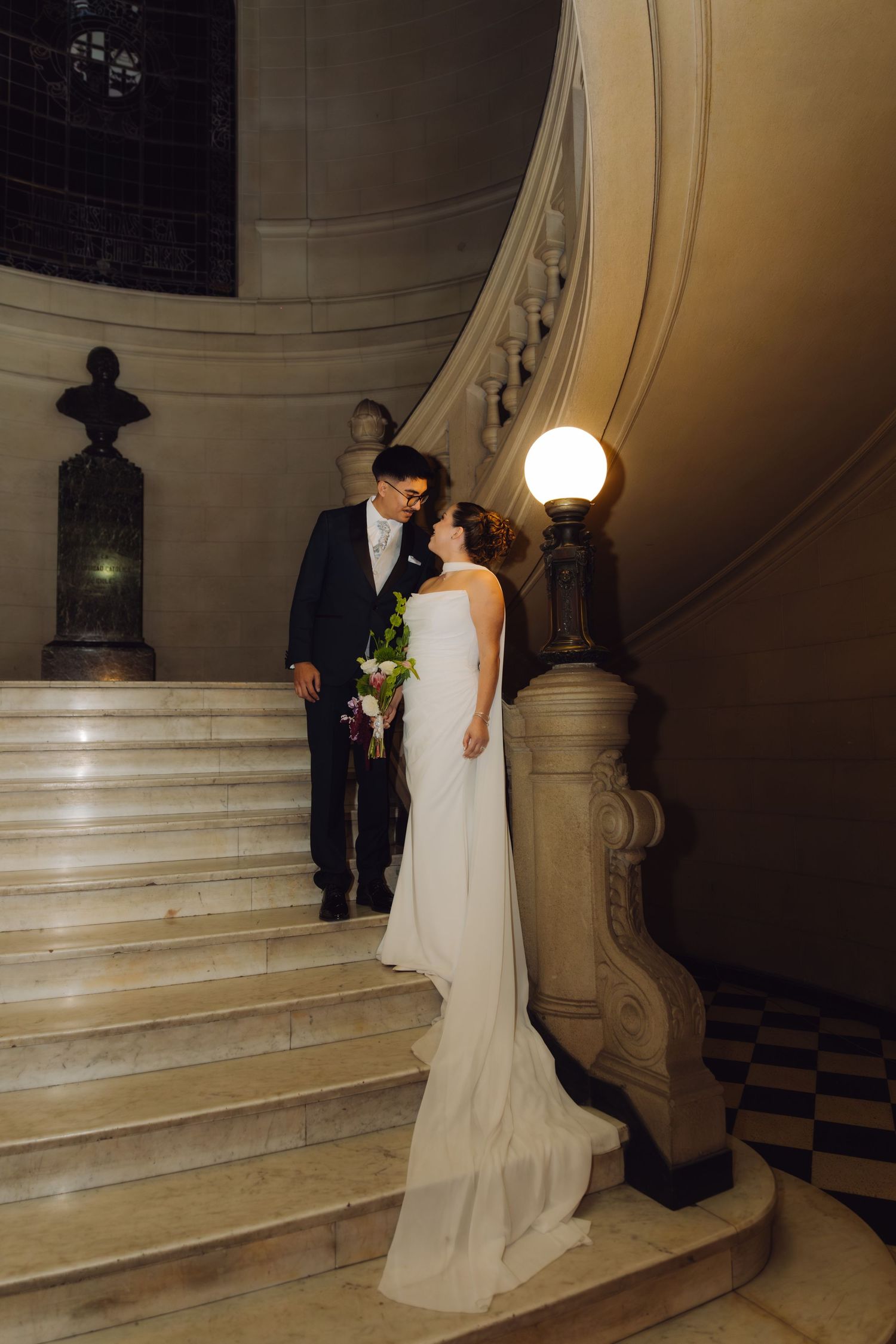 Bride holding bouquet and groom sharing a romantic moment on an ornate marble staircase.