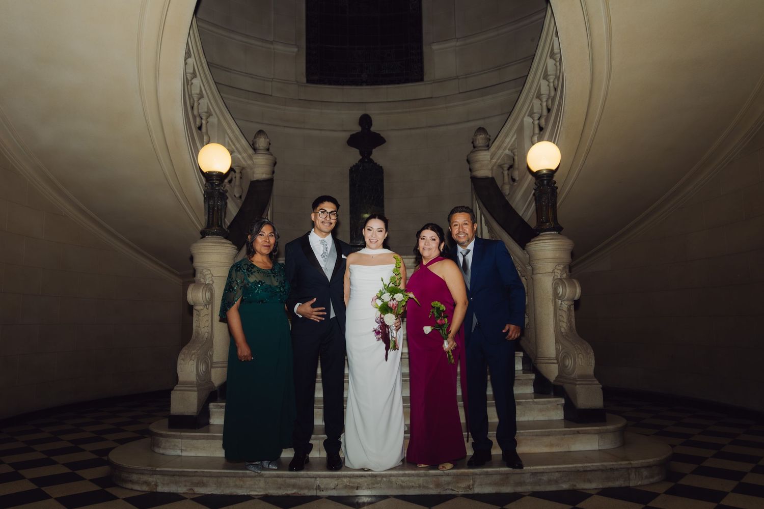 Wedding party of five posing on grand marble staircase at elegant evening ceremony venue.