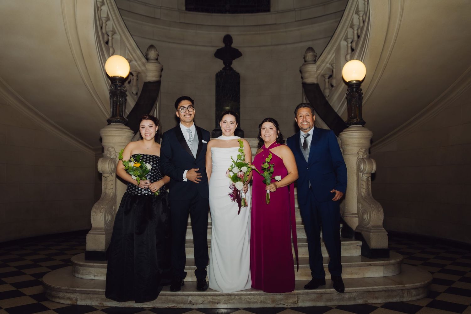 Wedding party group portrait on grand marble staircase with classical architecture at night.