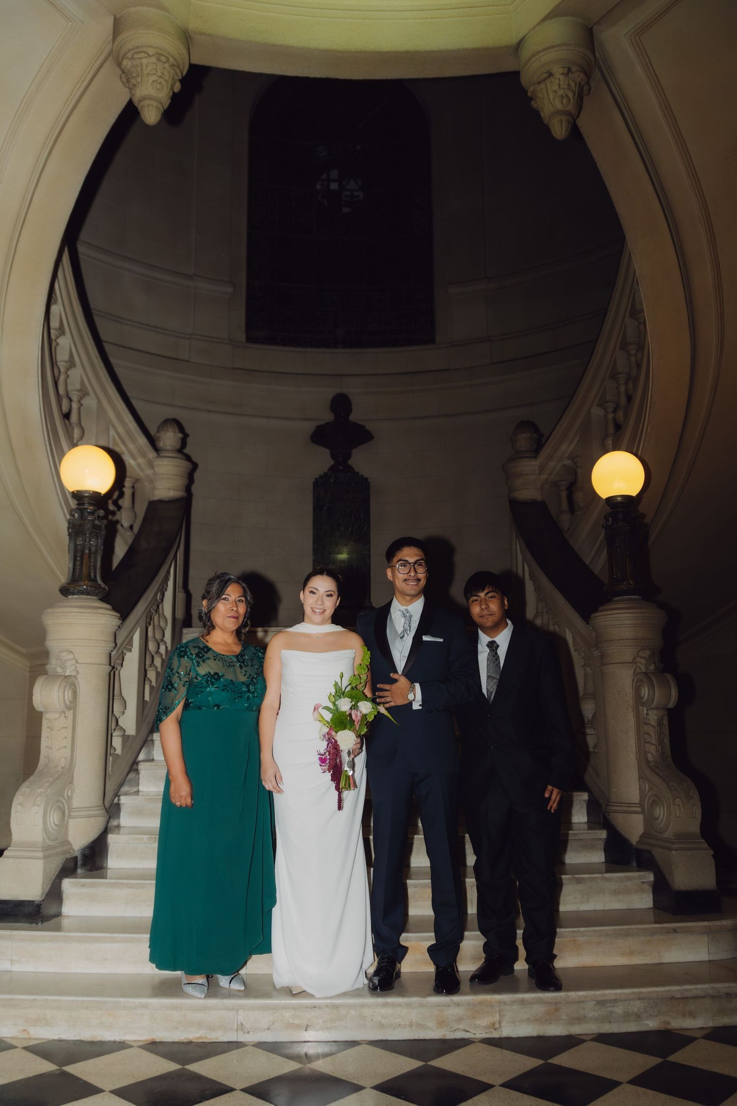 Bride and groom with family members posing on grand marble staircase at evening wedding.