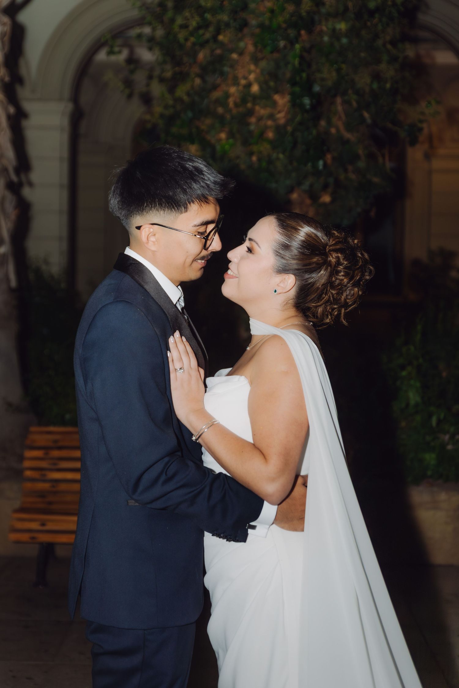 Wedding couple shares a romantic almost-kiss moment outdoors at night, bride in elegant white cape gown.