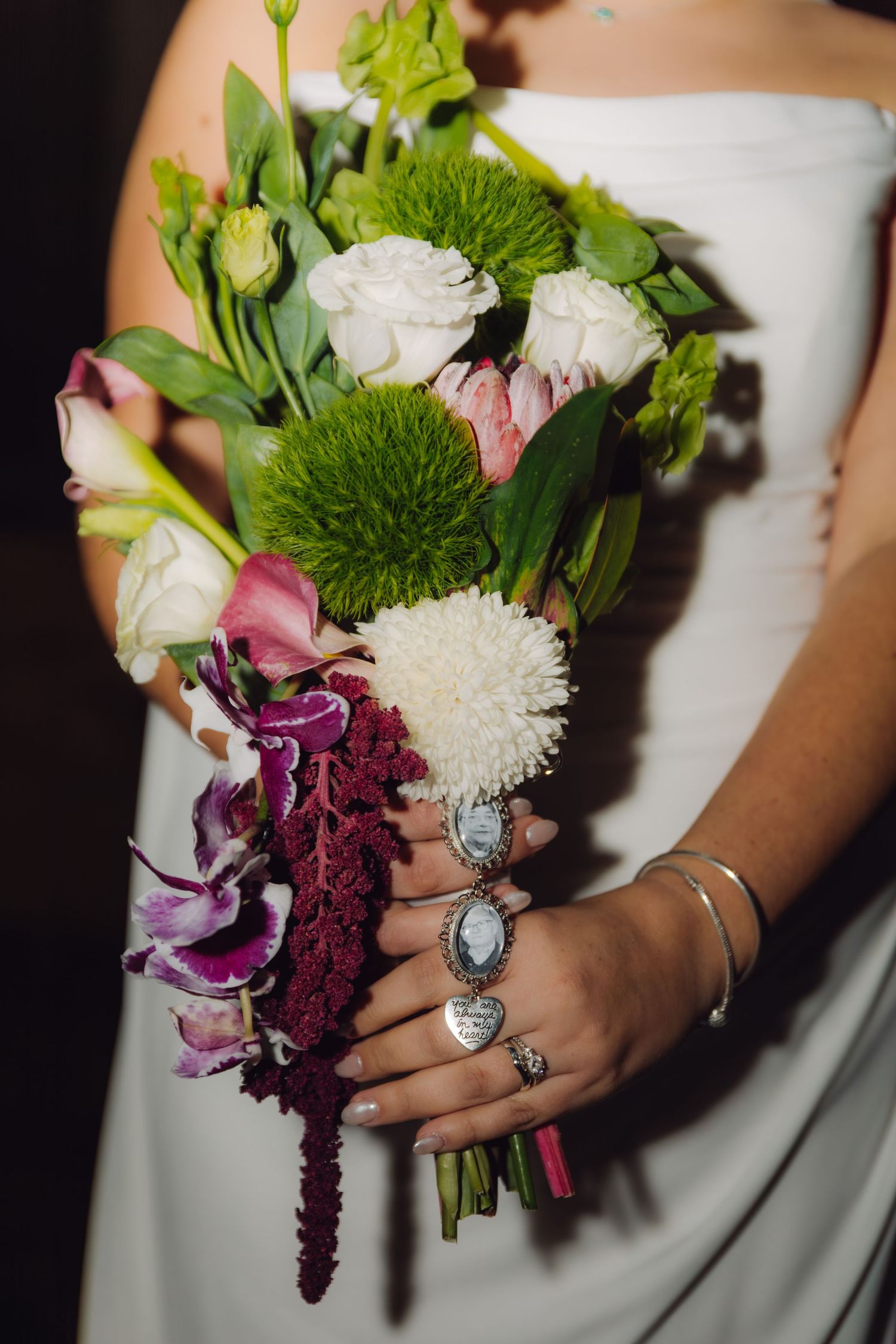 Close-up of bridal bouquet featuring white roses, green chrysanthemums, purple orchids, and burgundy amaranth.