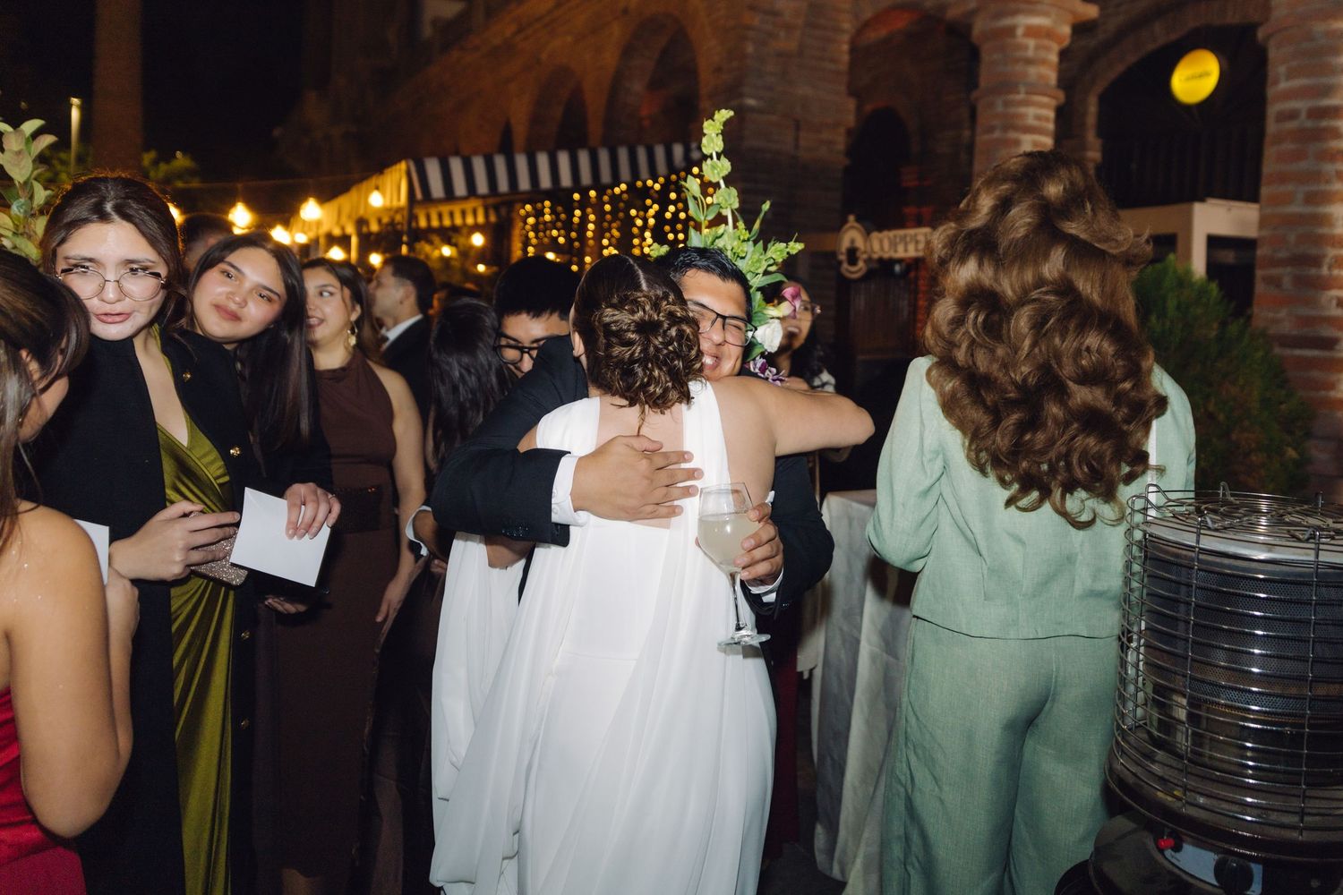 Wedding guests embracing and celebrating with the groom at an outdoor nighttime reception with warm lighting.