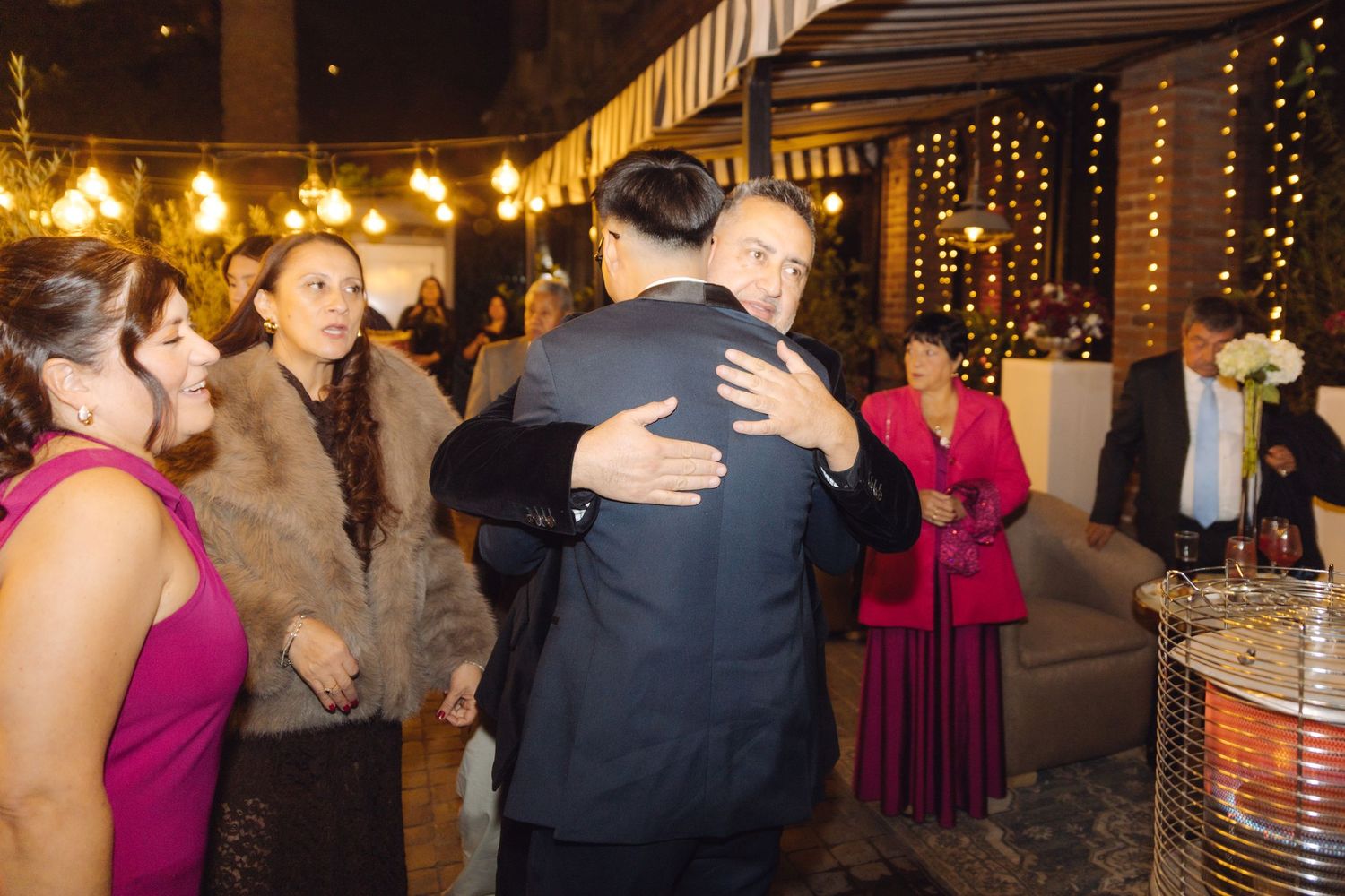 Guests hugging and socializing at an elegant outdoor evening wedding reception with warm ambient lighting.