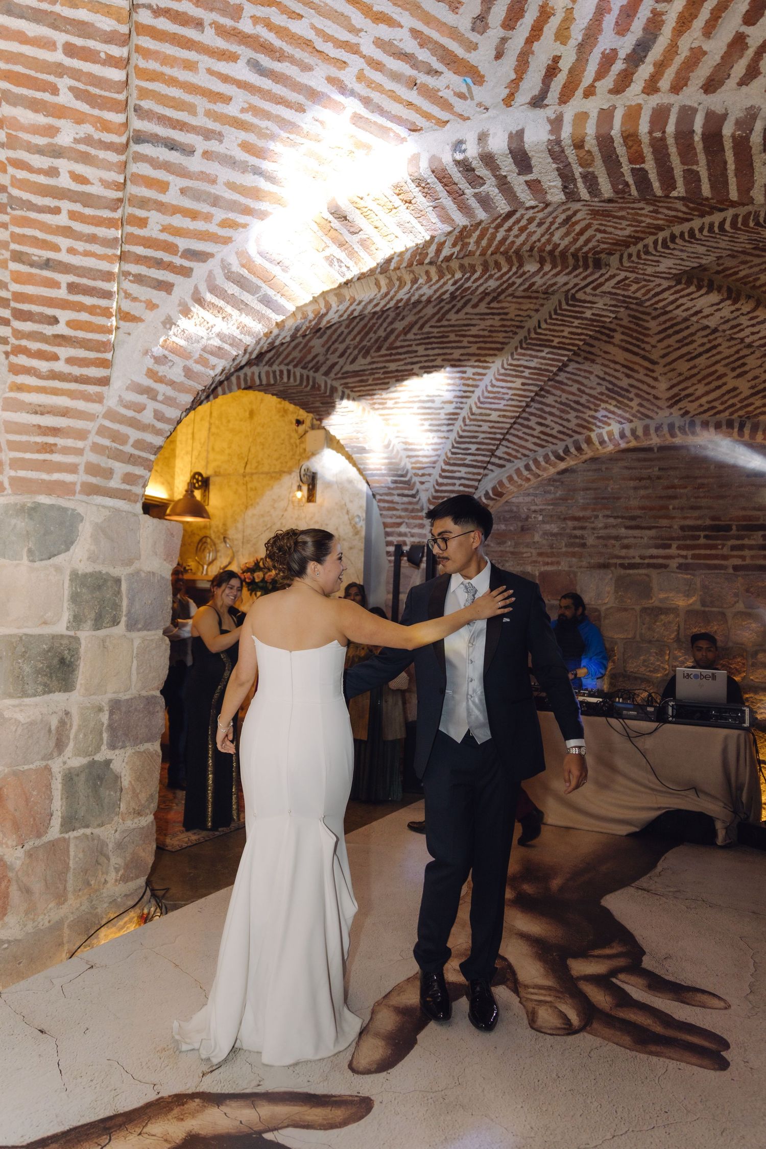 Bride and groom share their first dance under brick arched ceiling at elegant wedding reception venue.