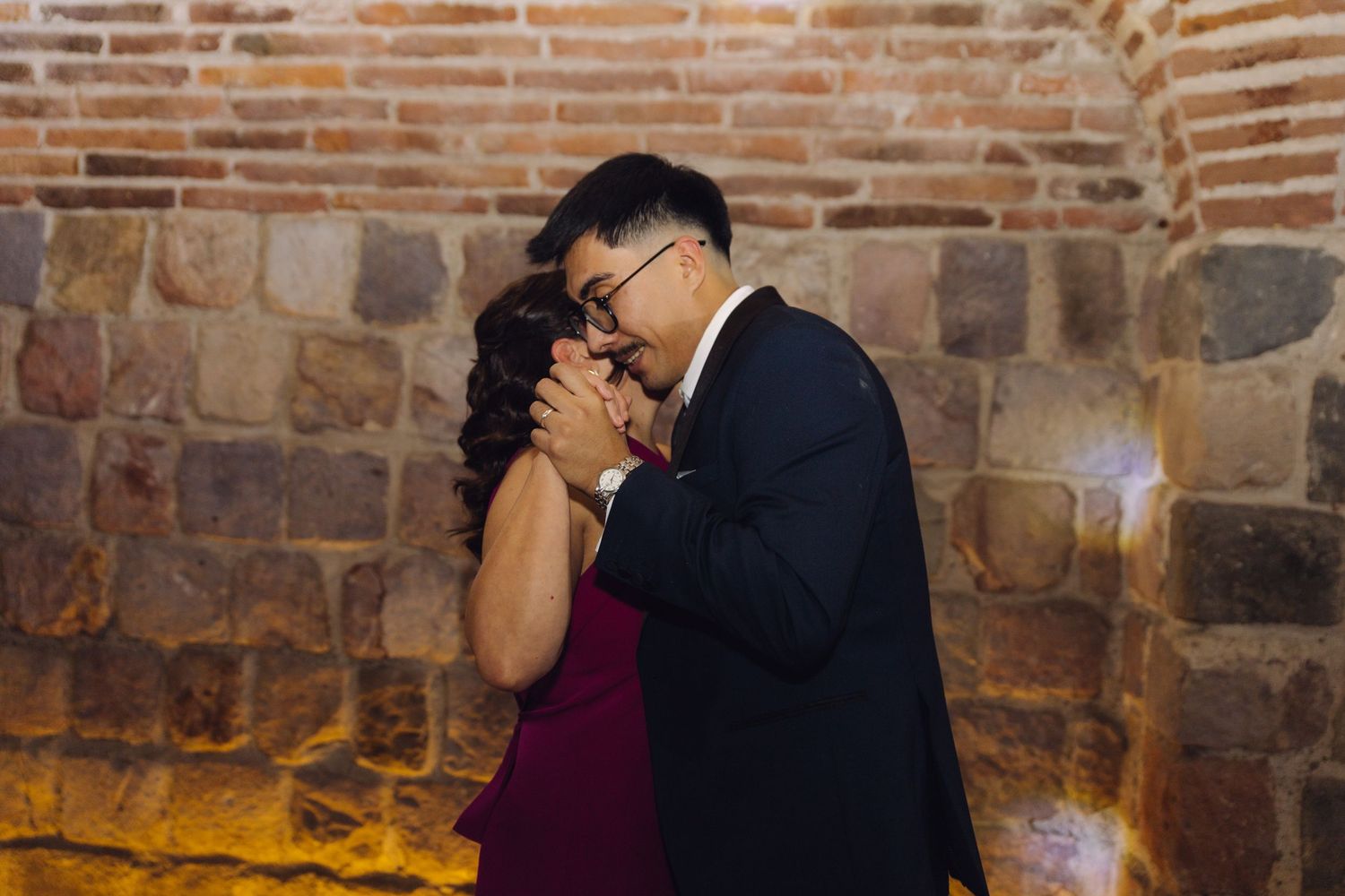 Couple sharing an intimate dance moment against a rustic brick wall at a wedding reception.