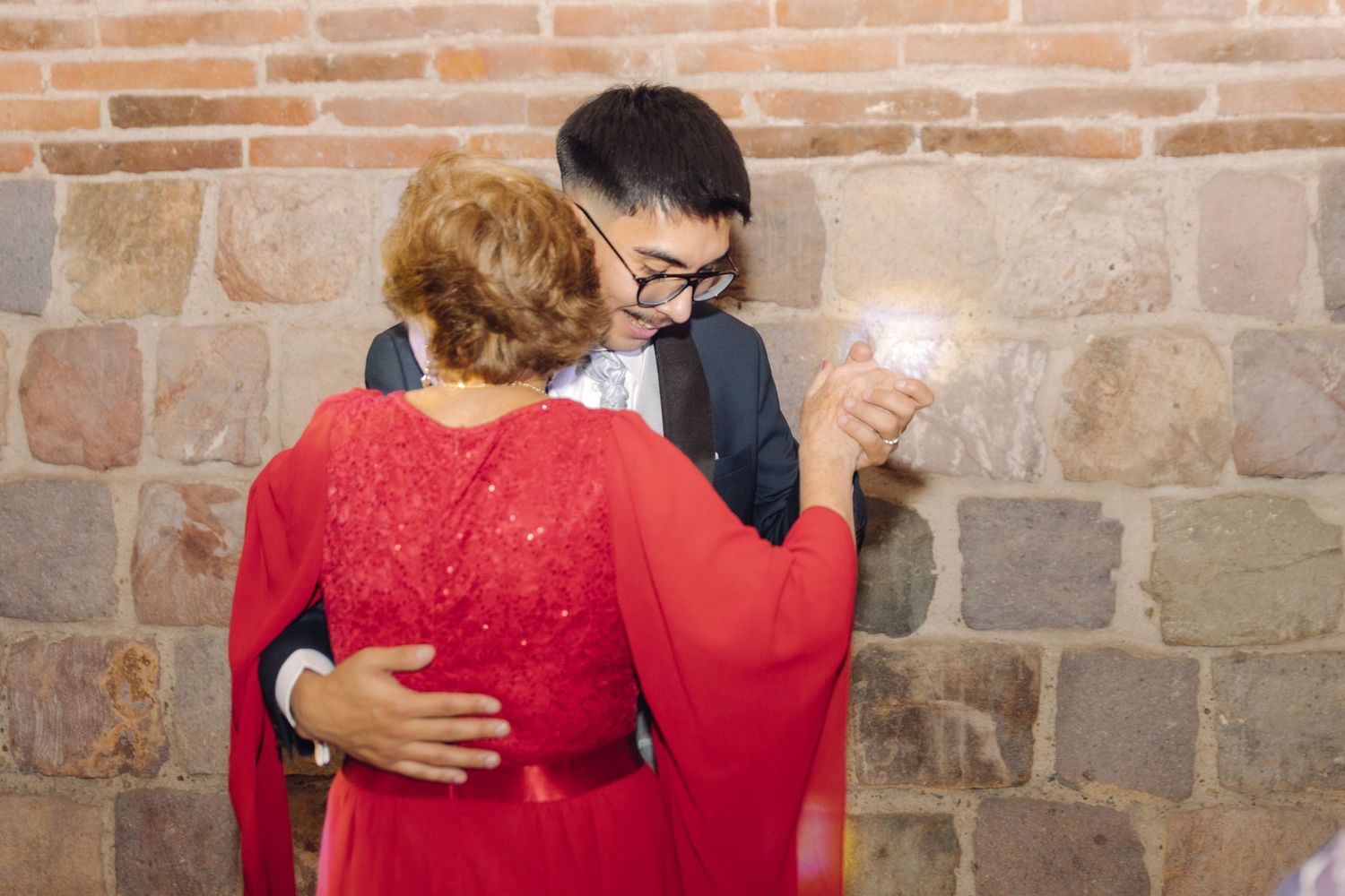 Groom in suit shares close dance with woman in red dress at wedding.