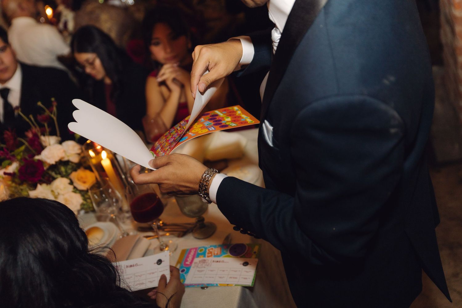 Wedding guest receiving colorful bingo card at festive reception dinner table.