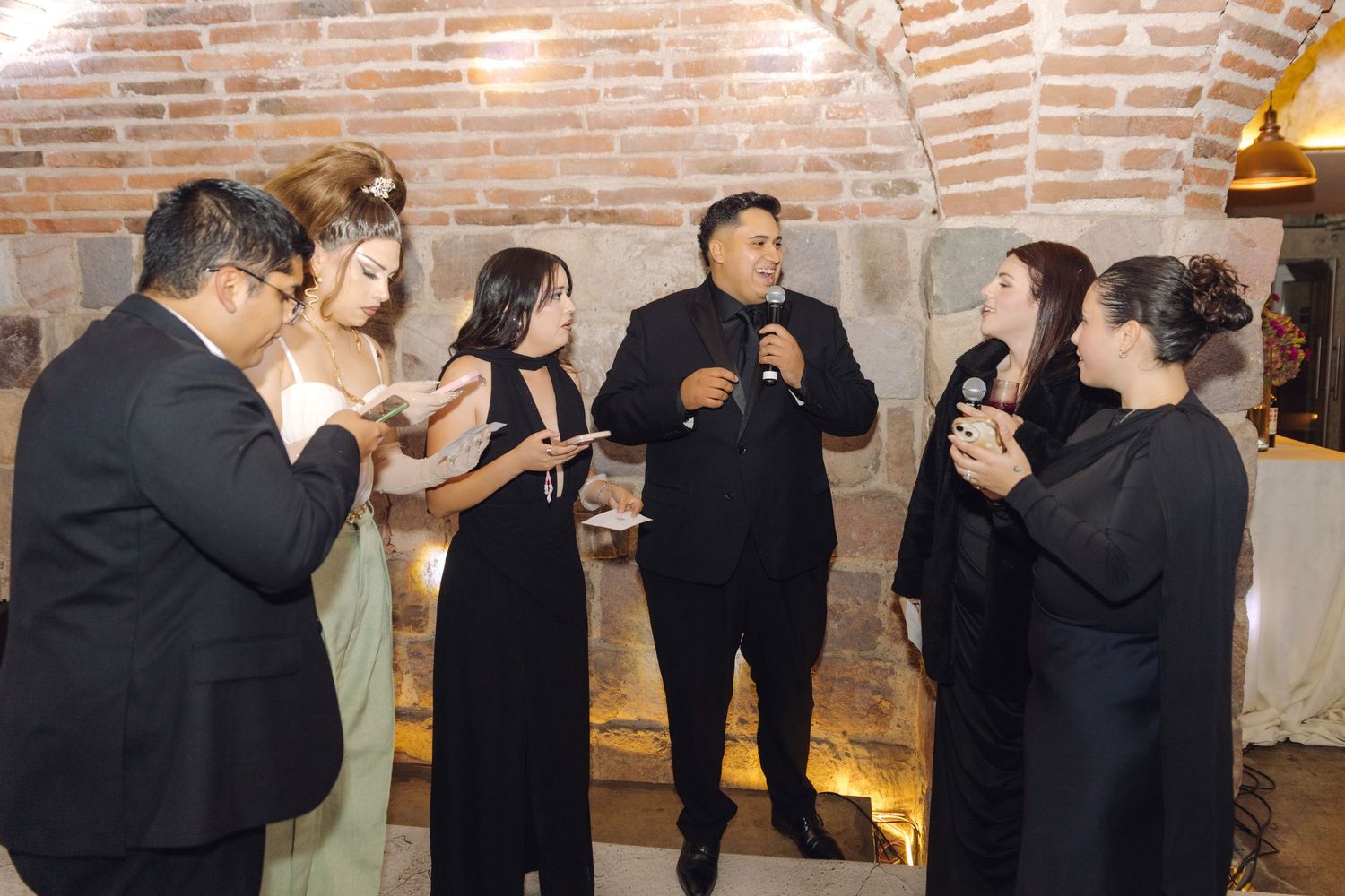 Group of wedding guests socializing and laughing together in rustic brick venue.