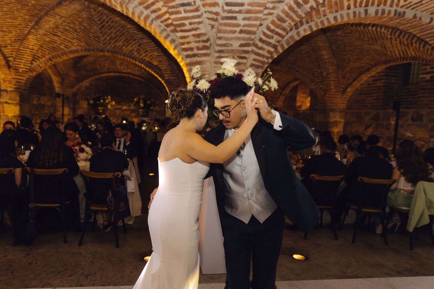 Bride and groom share an intimate first dance in a beautifully lit historic brick arched wedding venue.