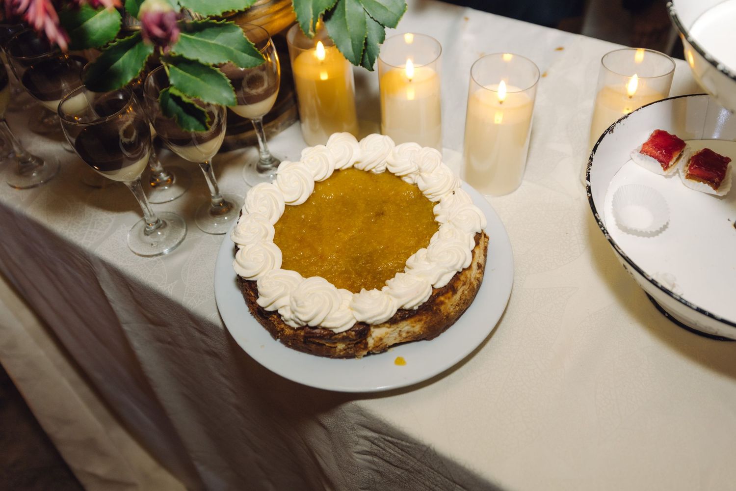 Elegant pumpkin pie with whipped cream rosettes displayed on a wedding dessert table with glowing candles.