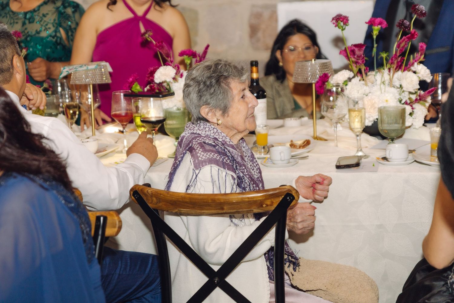 Elderly woman enjoying a wedding reception dinner at a elegantly decorated table with floral centerpieces.