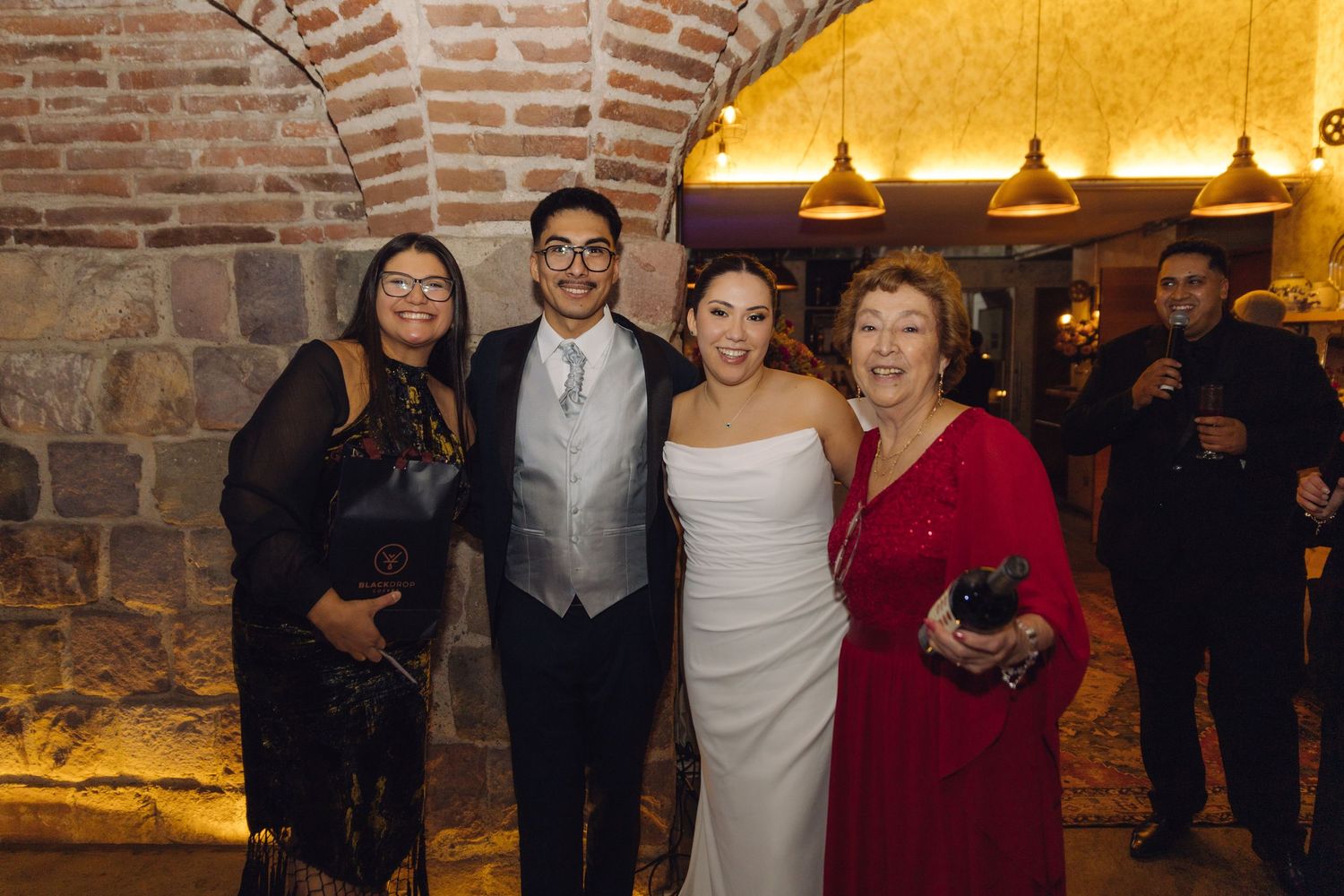 Bride and groom posing with two female family members at their wedding reception in a brick venue.