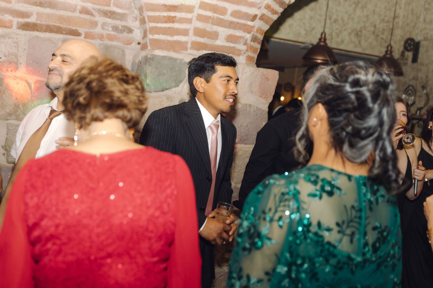 Guests in formal attire socializing at an elegant wedding reception in a rustic stone venue.