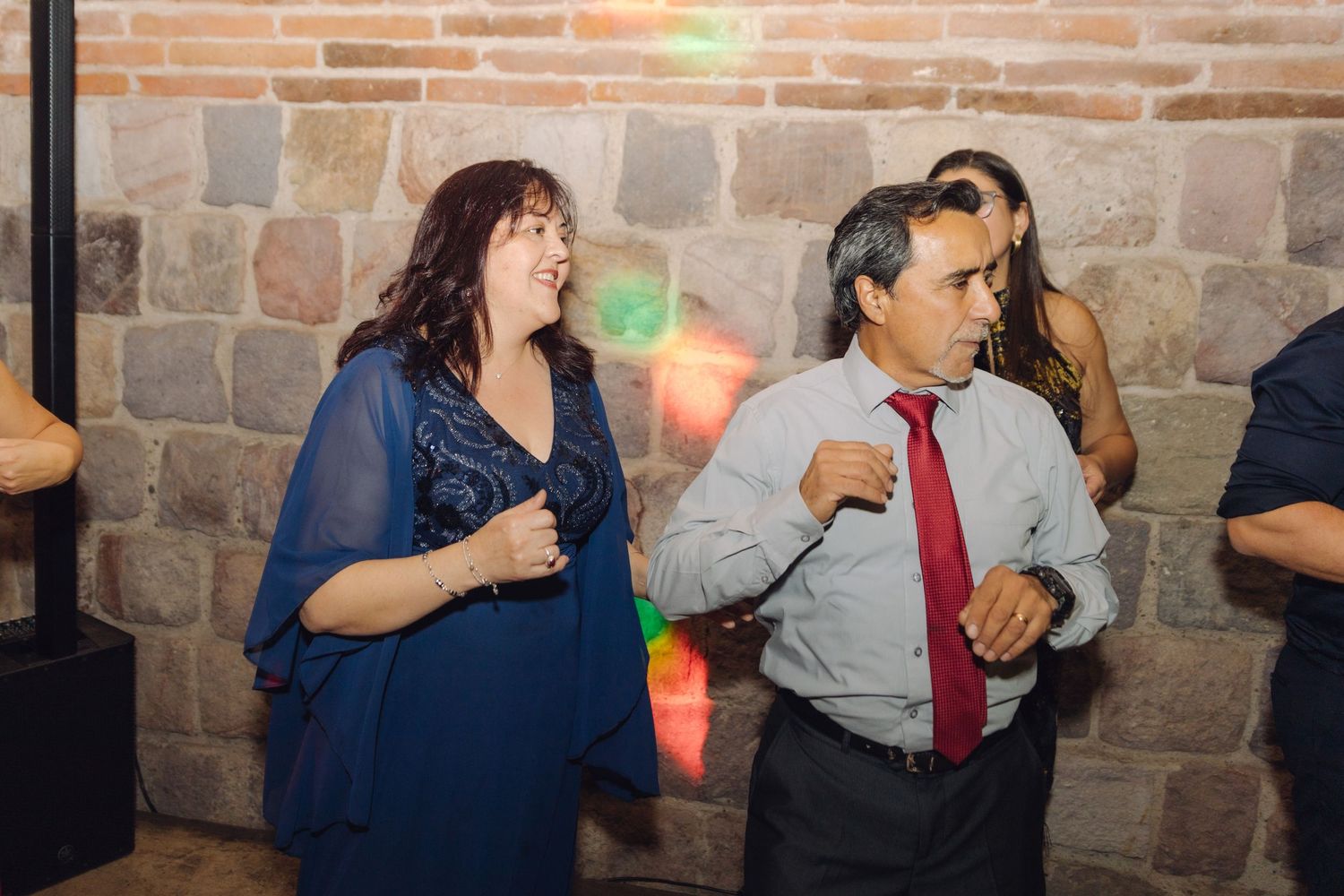 Couple dancing together at a wedding reception, man in white shirt and red tie, woman in blue dress.