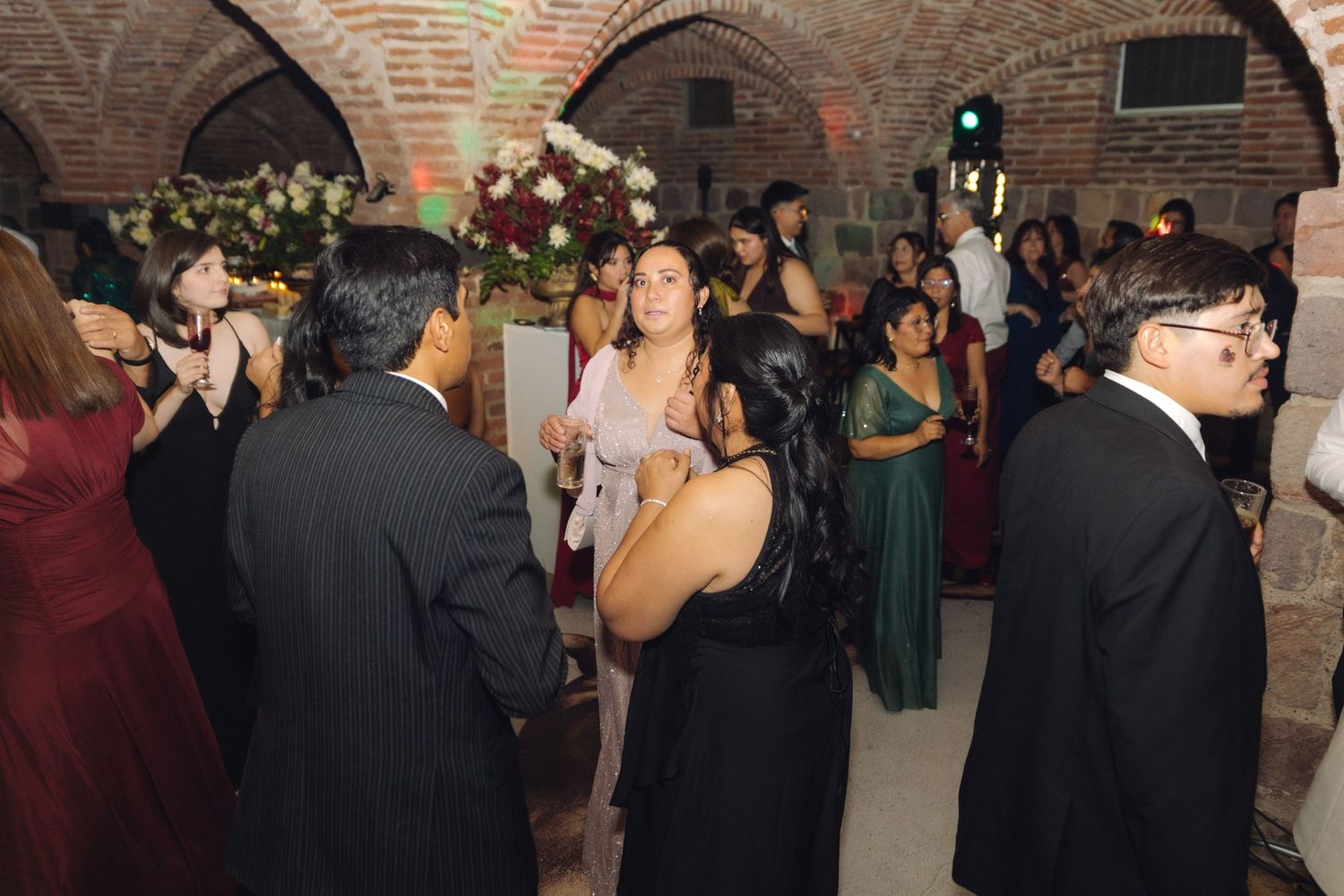 Formally dressed wedding guests mingling and dancing under arched brick ceilings at a reception.