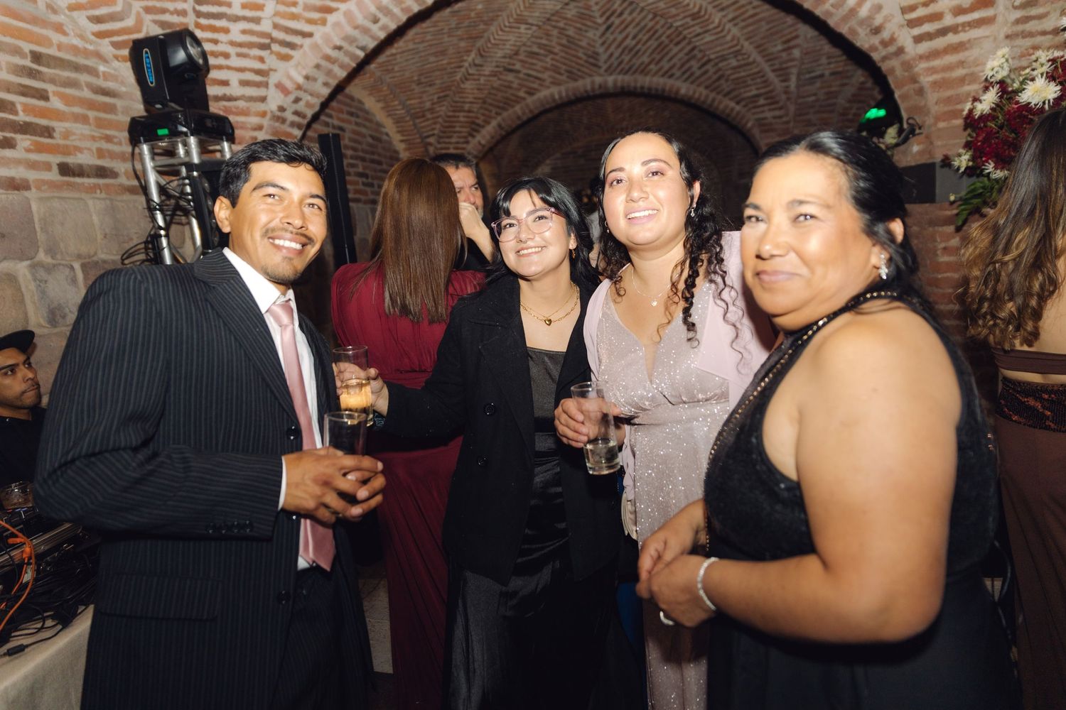 Four formally dressed guests posing and smiling together at a wedding reception in a stone venue.