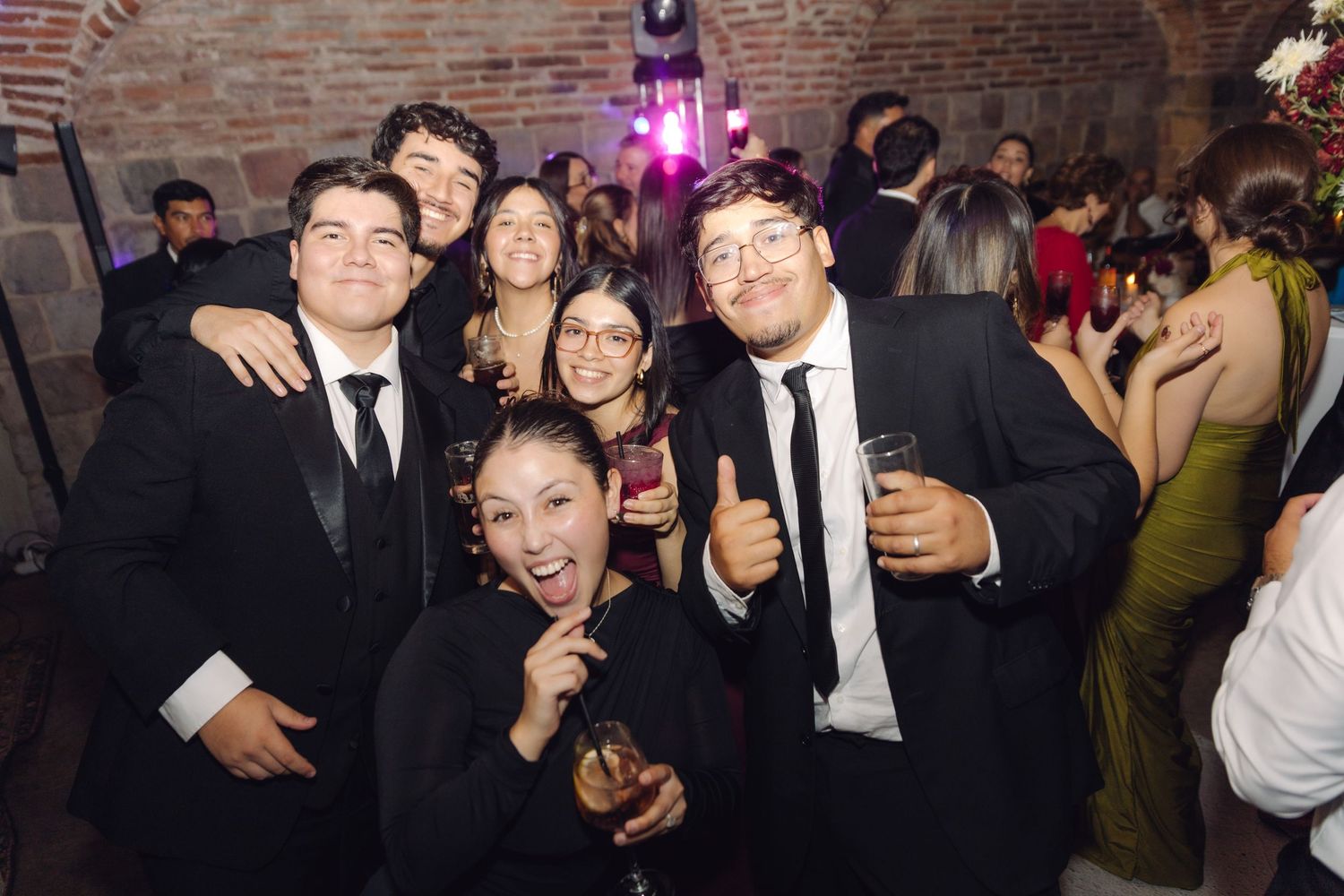 Cheerful group of wedding guests in black formal attire posing together at a festive reception.