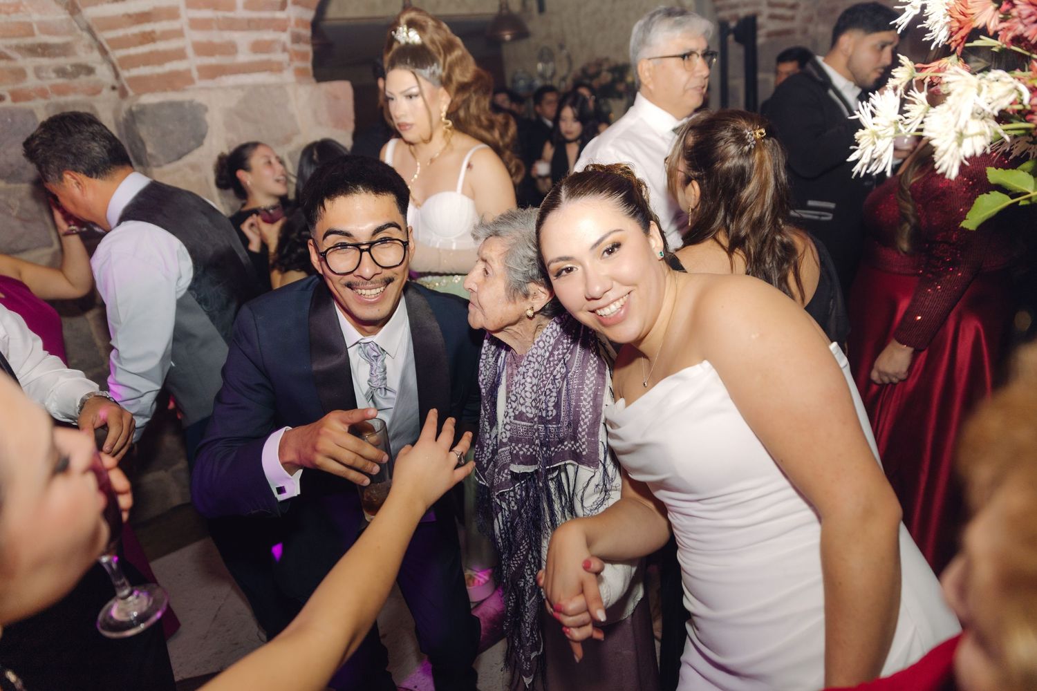 Bride in white dress posing with guests including a man in suit at a lively wedding reception.