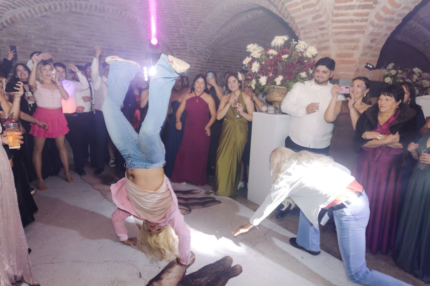 A woman does a headstand on the dance floor while guests cheer at a wedding reception.