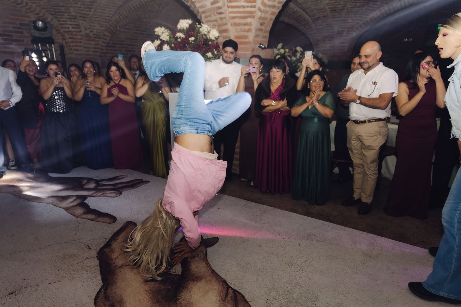 A woman executes an impressive headstand on the dance floor surrounded by wedding guests.