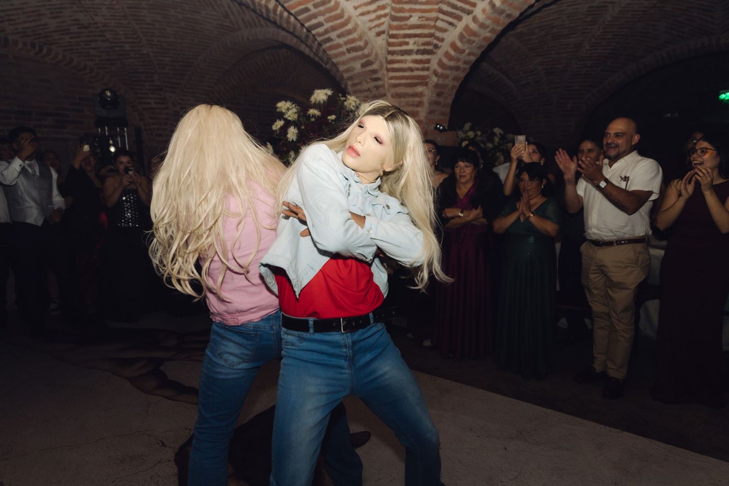 Two blonde women in jeans dance closely together at a wedding reception in a brick venue.