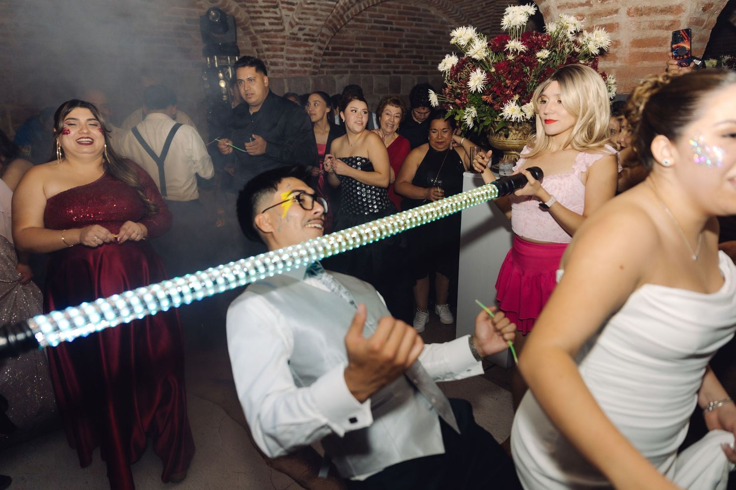 A wedding guest does the limbo under a light-up bar at a lively wedding reception.