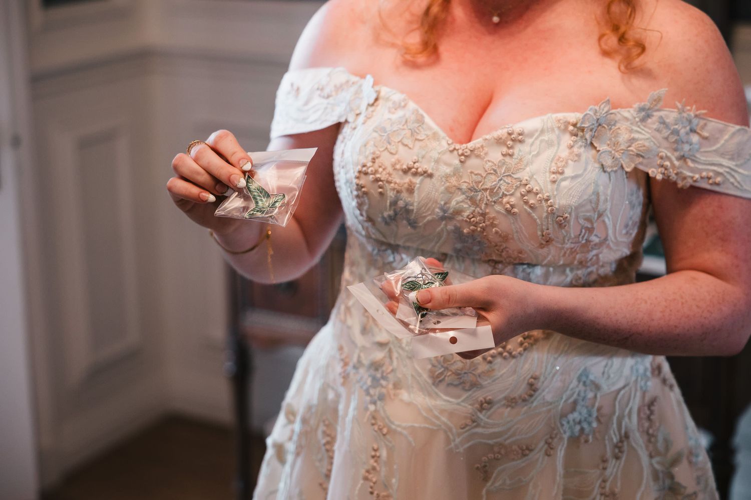 Close-up of the bride's hands holding two packaged elf leaf pins, a gift for her bridal party, at Searles Castle.