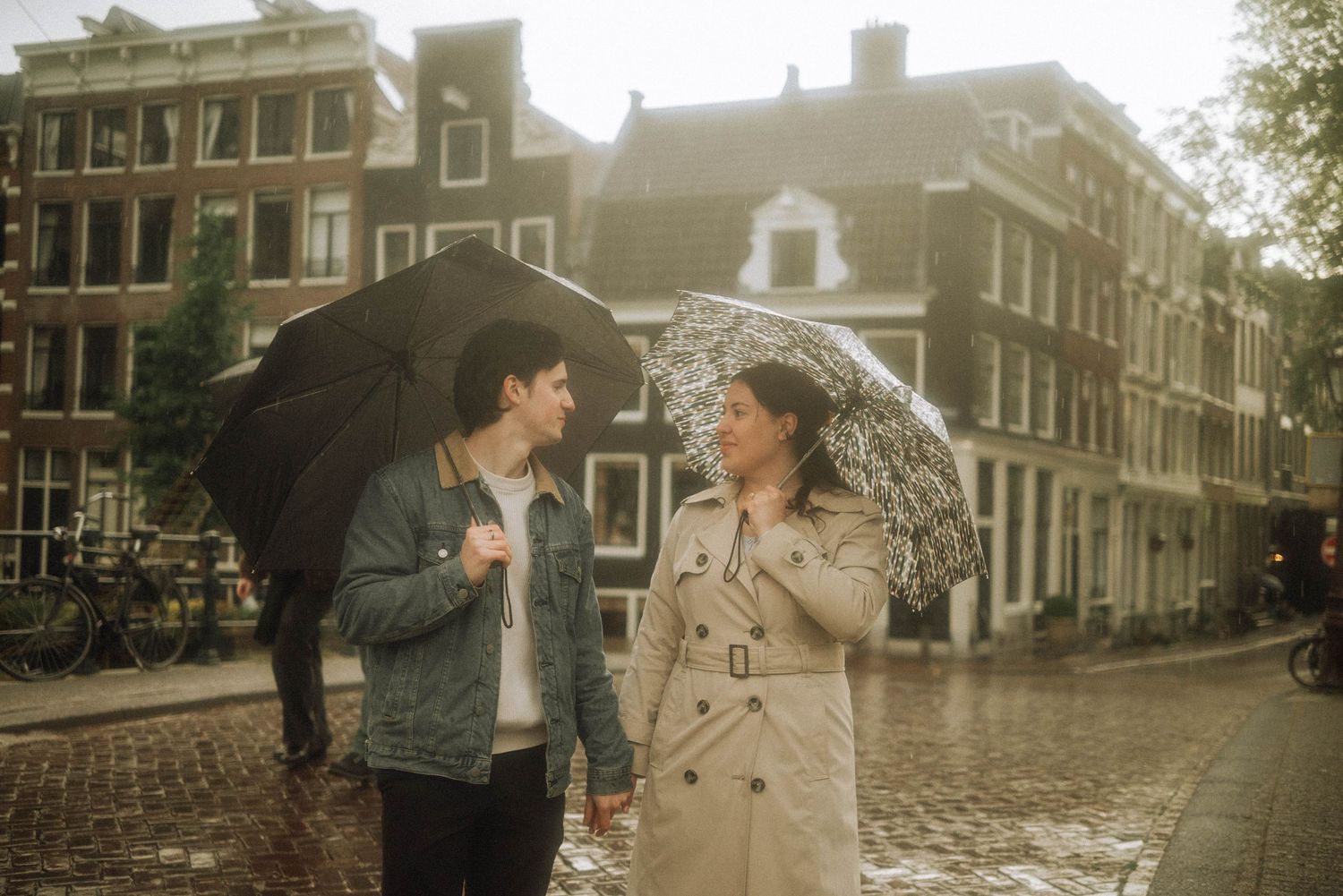 Couple sharing umbrellas in the rain on a cobblestone street in Amsterdam, Netherlands.