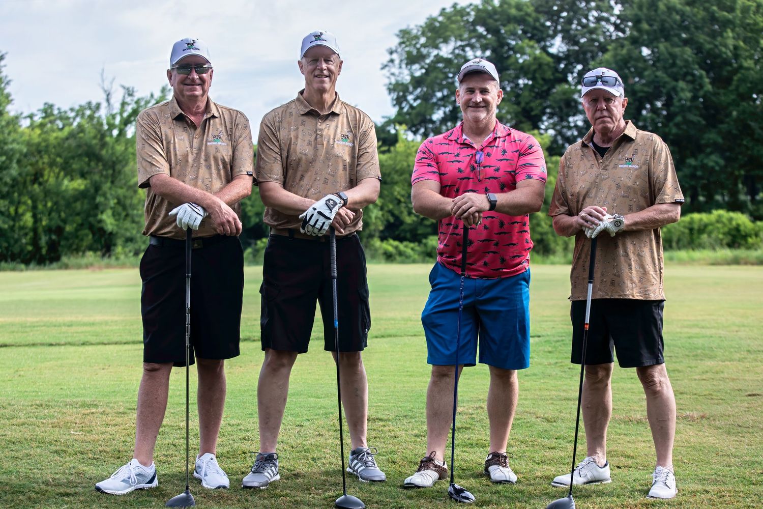 Four male golfers posing together on a golf course, holding clubs and smiling outdoors.