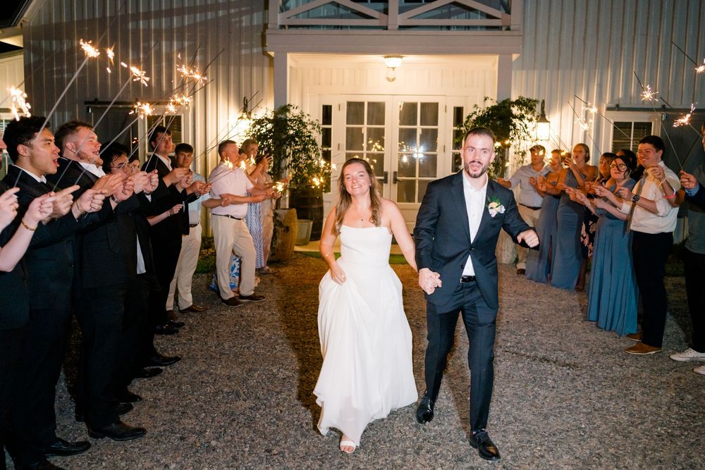 Bride and groom exit wedding venue through sparkler tunnel at night.