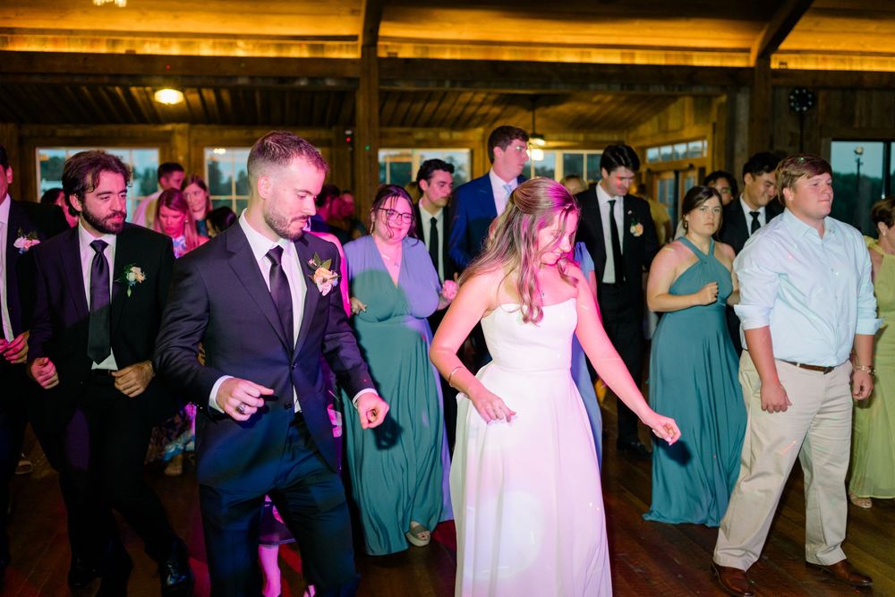 Bride and groom dancing joyfully with guests at wedding reception in rustic venue.