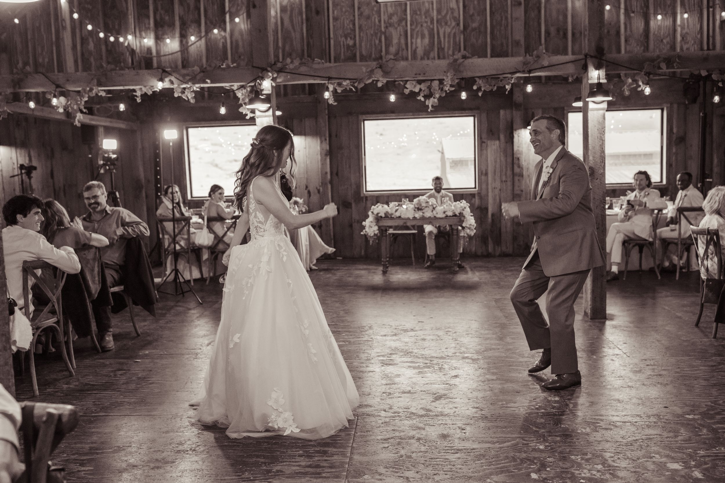 Bride and groom share lively first dance in rustic barn venue surrounded by wedding guests.